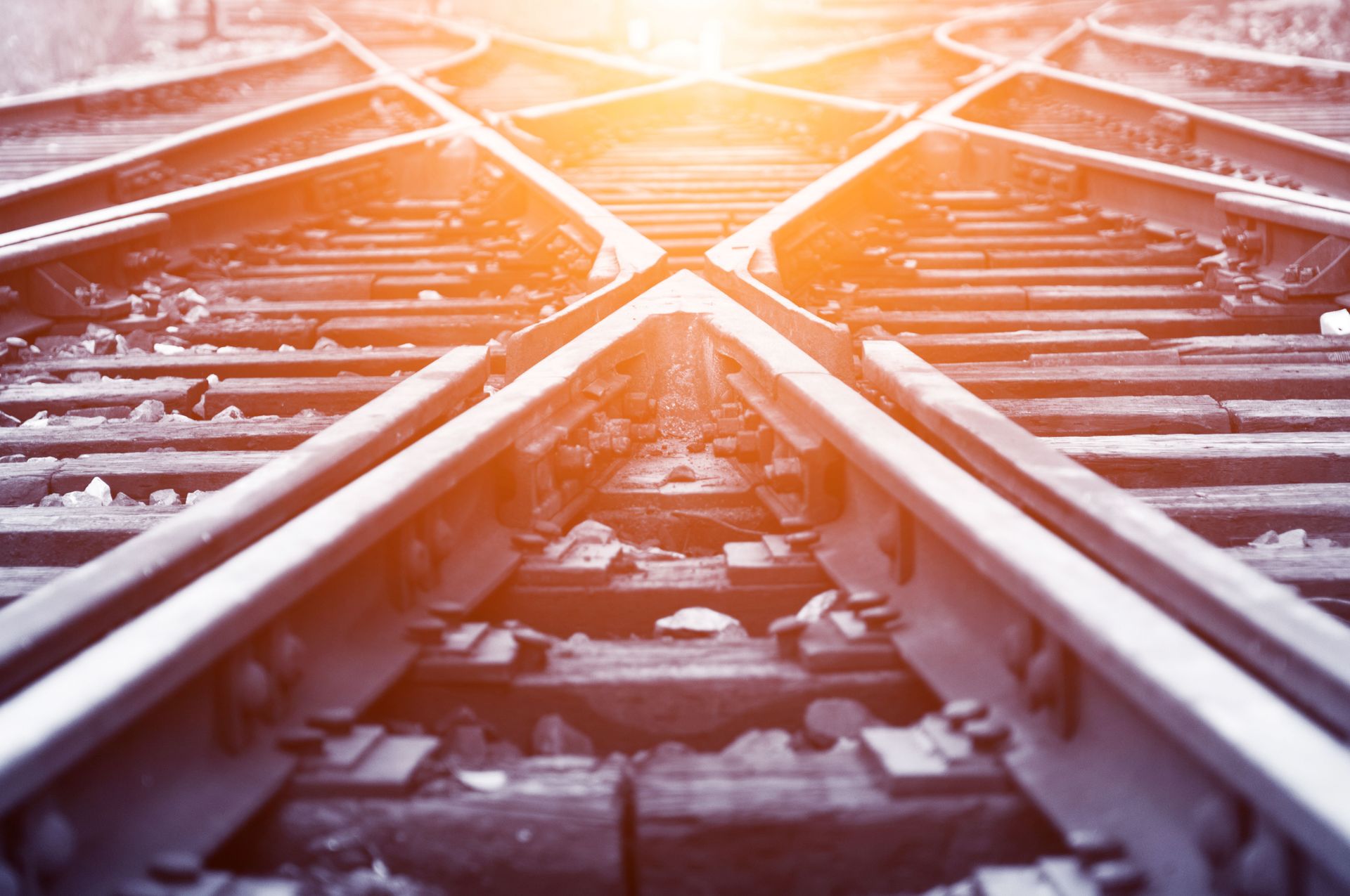 Una vista dal basso di binari ferroviari che si intersecano e conducono verso un orizzonte luminoso e soleggiato.