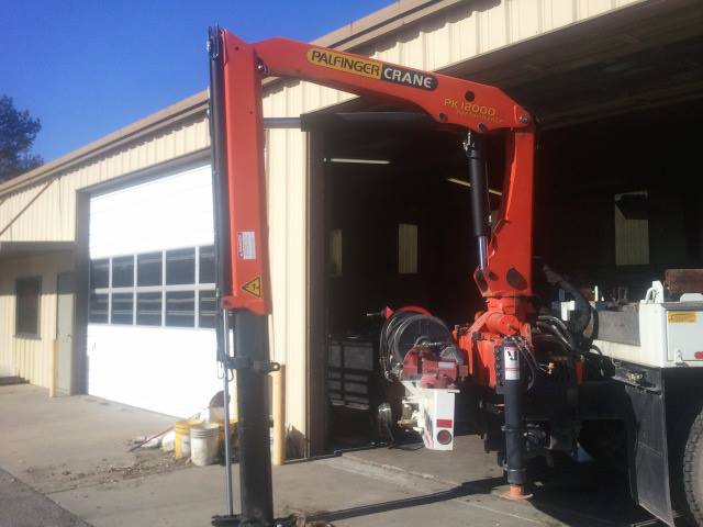 Orange Palfinger crane mounted on a truck bed, in front of a garage with a white door.