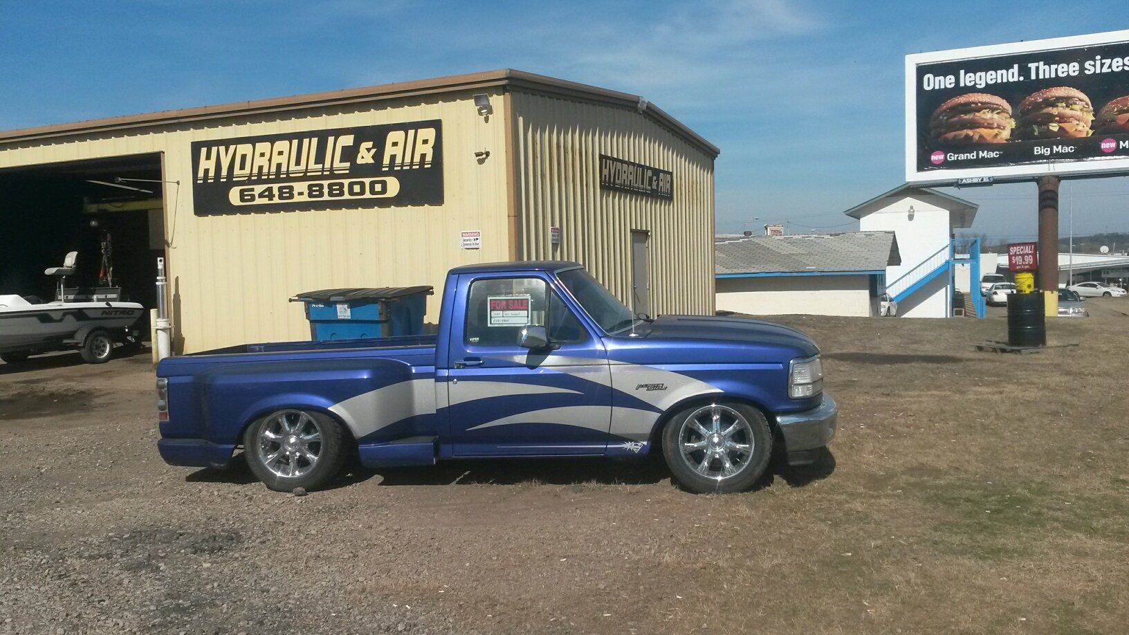 Blue custom truck parked in front of a shop with a sign