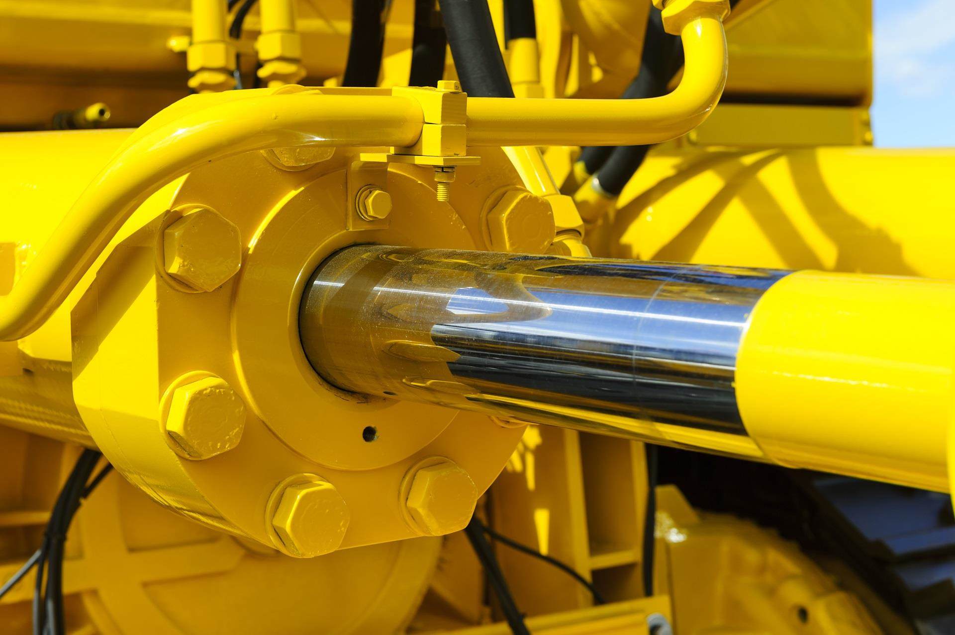 Close-up of a shiny chrome hydraulic cylinder with a bright yellow metal housing and bolts.