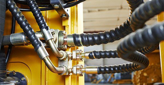 Close-up of hydraulic hoses and fittings connected to a yellow machine.