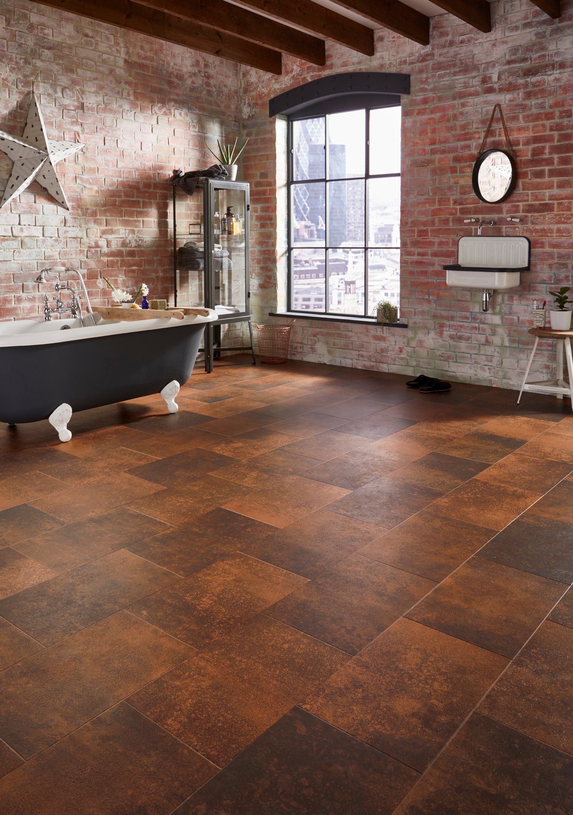 A brown tiled floor in a bathroom with a free standing bath and red brick walls