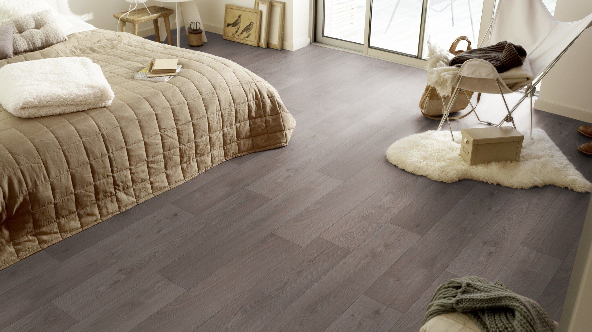 A wooden floor in a large bedroom with a large cream bed and decoration