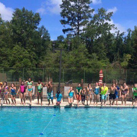 Group of people jumping into a blue outdoor pool on a sunny day.