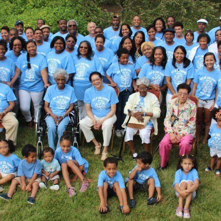 Large group of people in light blue shirts pose on a grassy lawn.