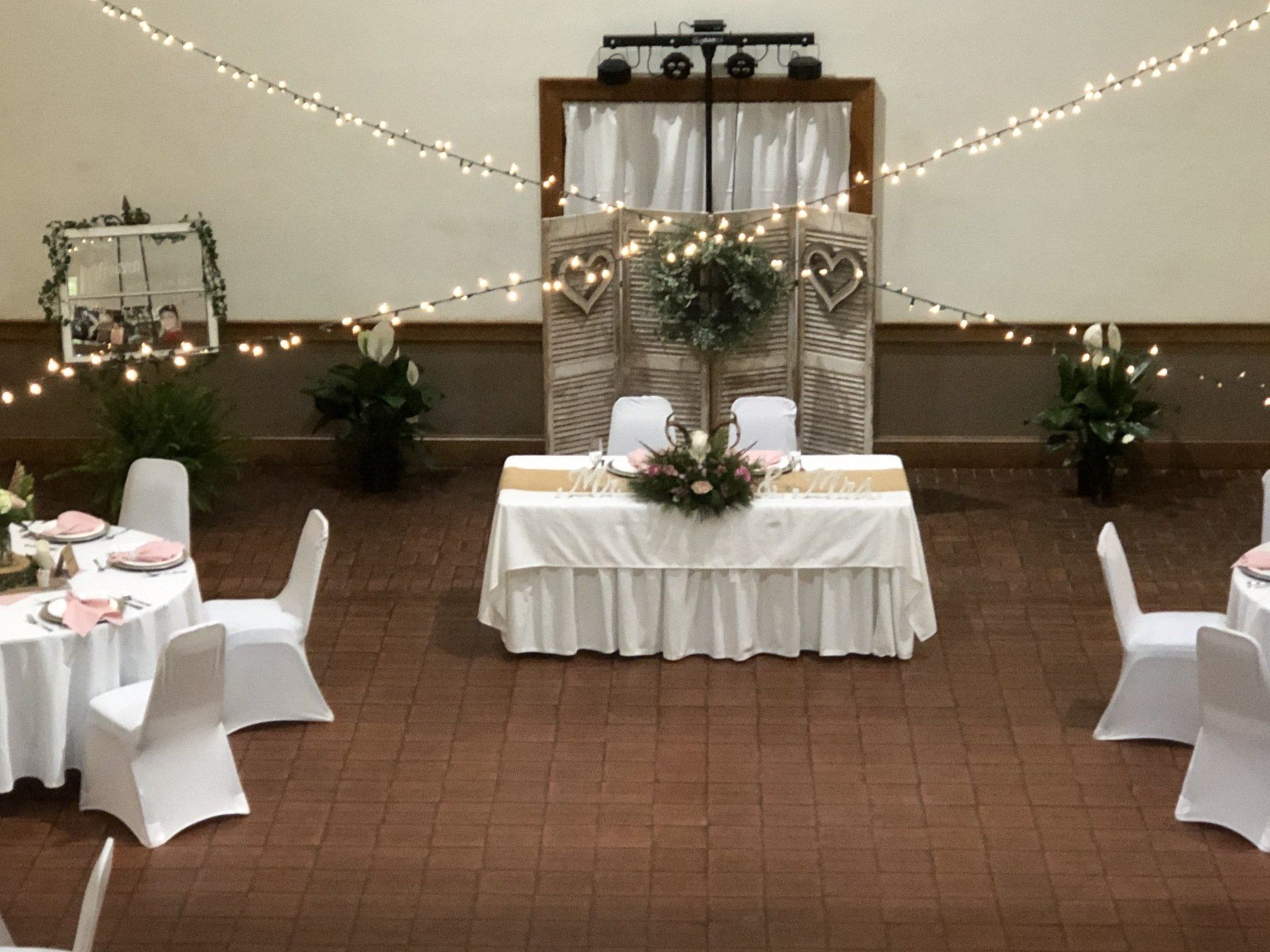 Wedding reception hall, decorated with string lights, floral centerpieces, and white tablecloths.