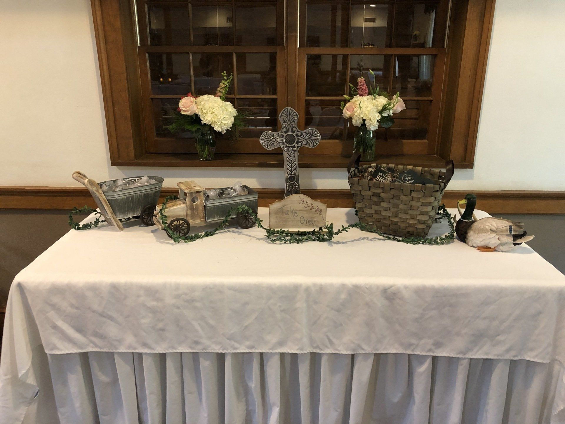 A table draped in white cloth is decorated with flowers, a cross, and decorative objects.