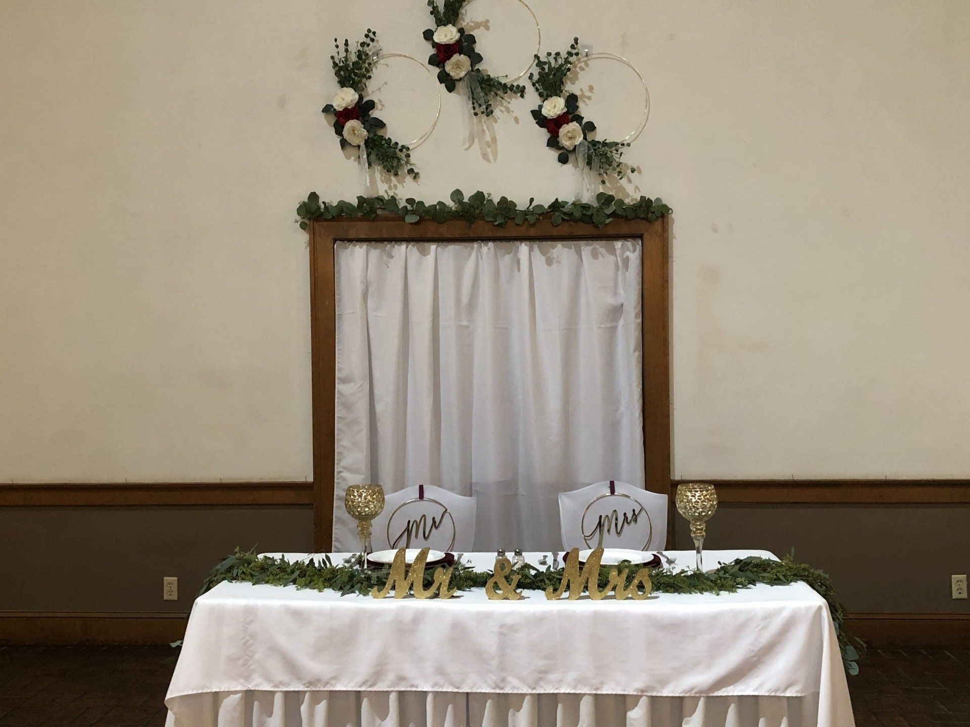 Wedding reception sweetheart table with decorations and hoop floral arrangements.