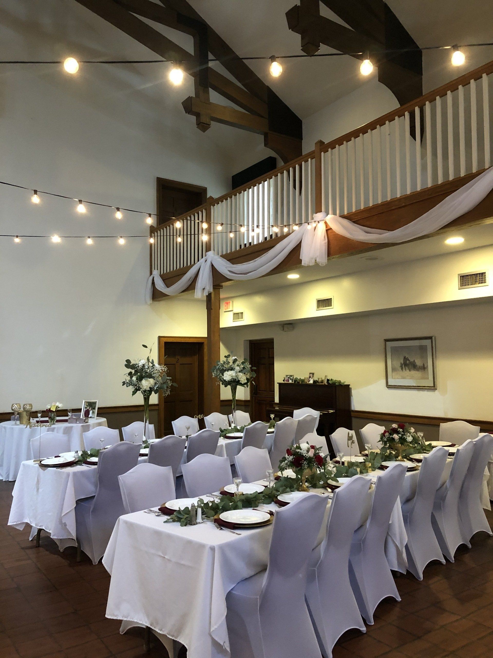 Wedding reception hall with tables set for guests, draped with fabric and floral centerpieces.