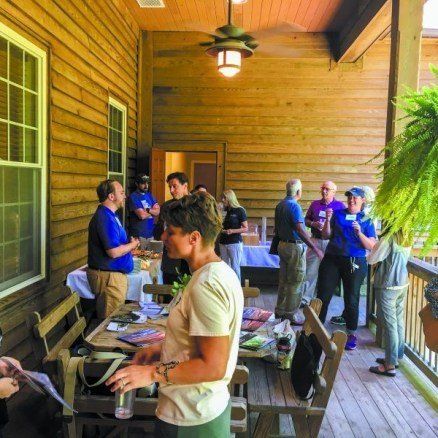 People socializing on a wooden porch with tables, drinks, and snacks.