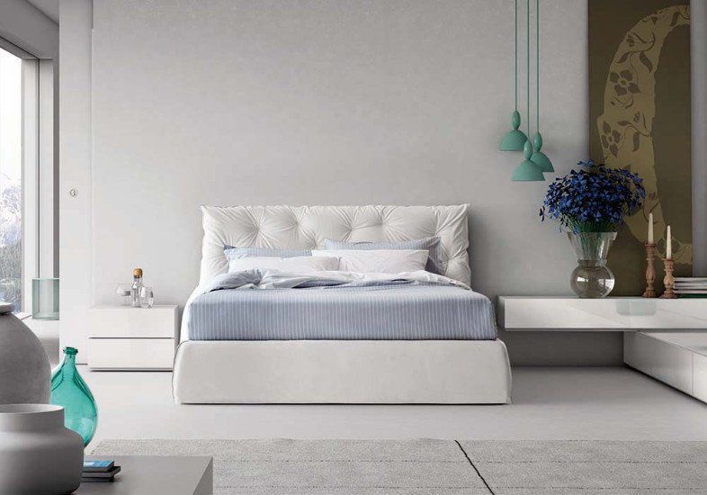 una camera con un letto bianco con la testata imbottita e dei comodini a muro