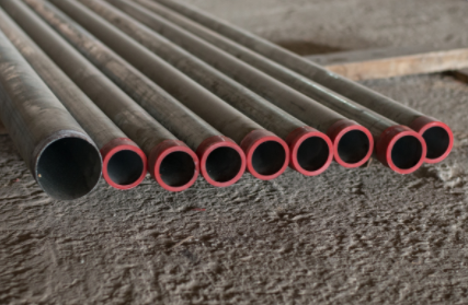 Stacked metal pipes with red rims lying on a rough surface