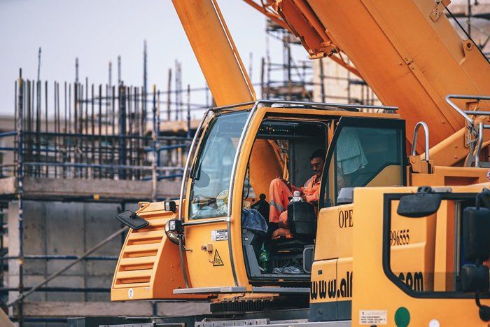 A man is sitting in the driver 's seat of a yellow construction crane.