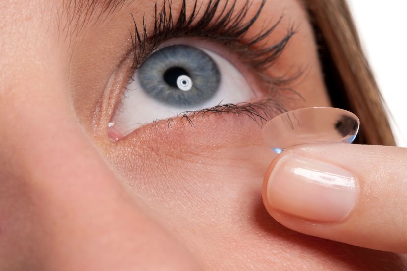 Ein Finger hält eine klare Kontaktlinse in der Nähe eines blauen Auges und bereitet sie zum Einsetzen vor.