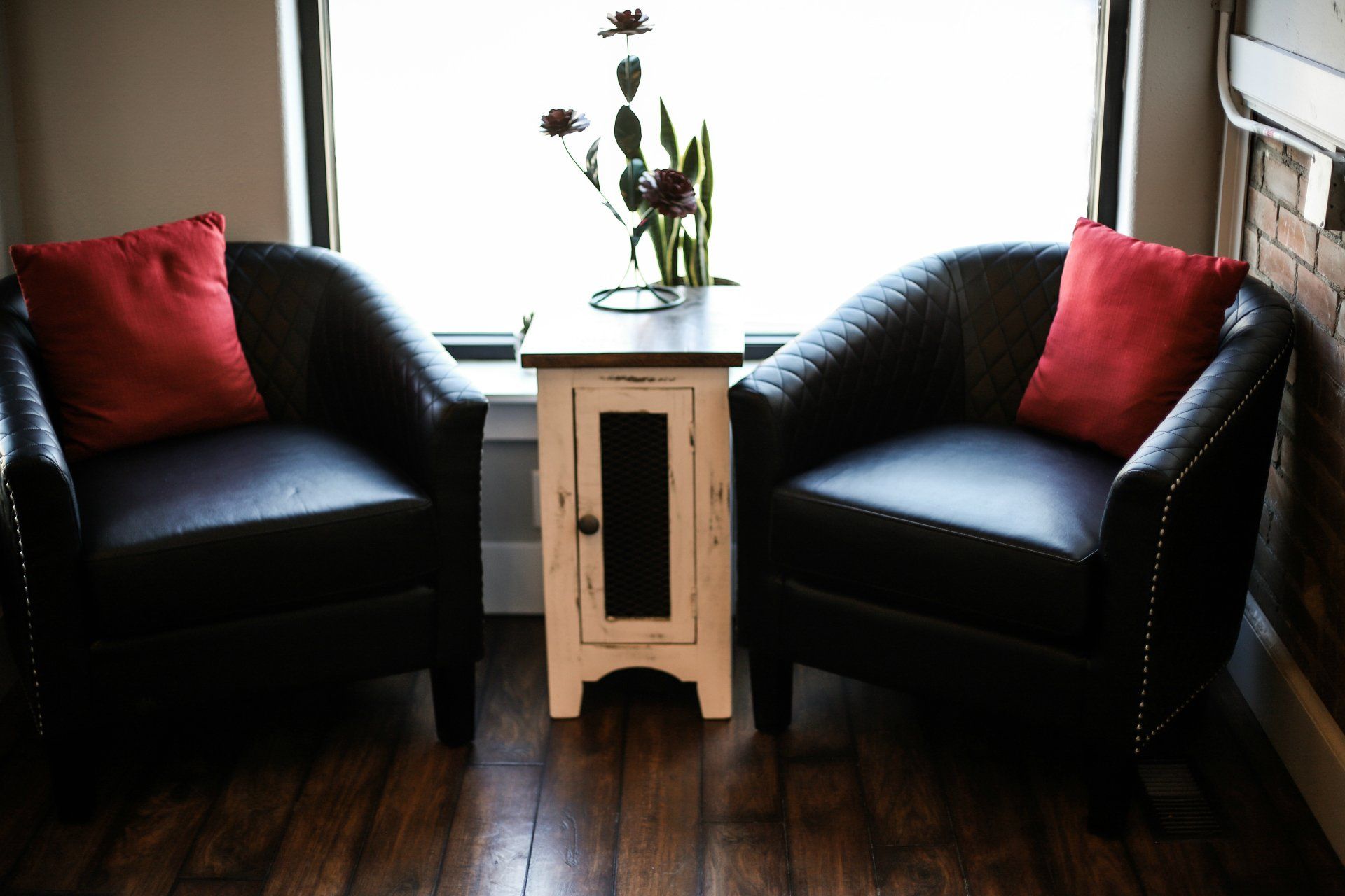 Two black armchairs with red pillows beside a small wooden table in a bright room