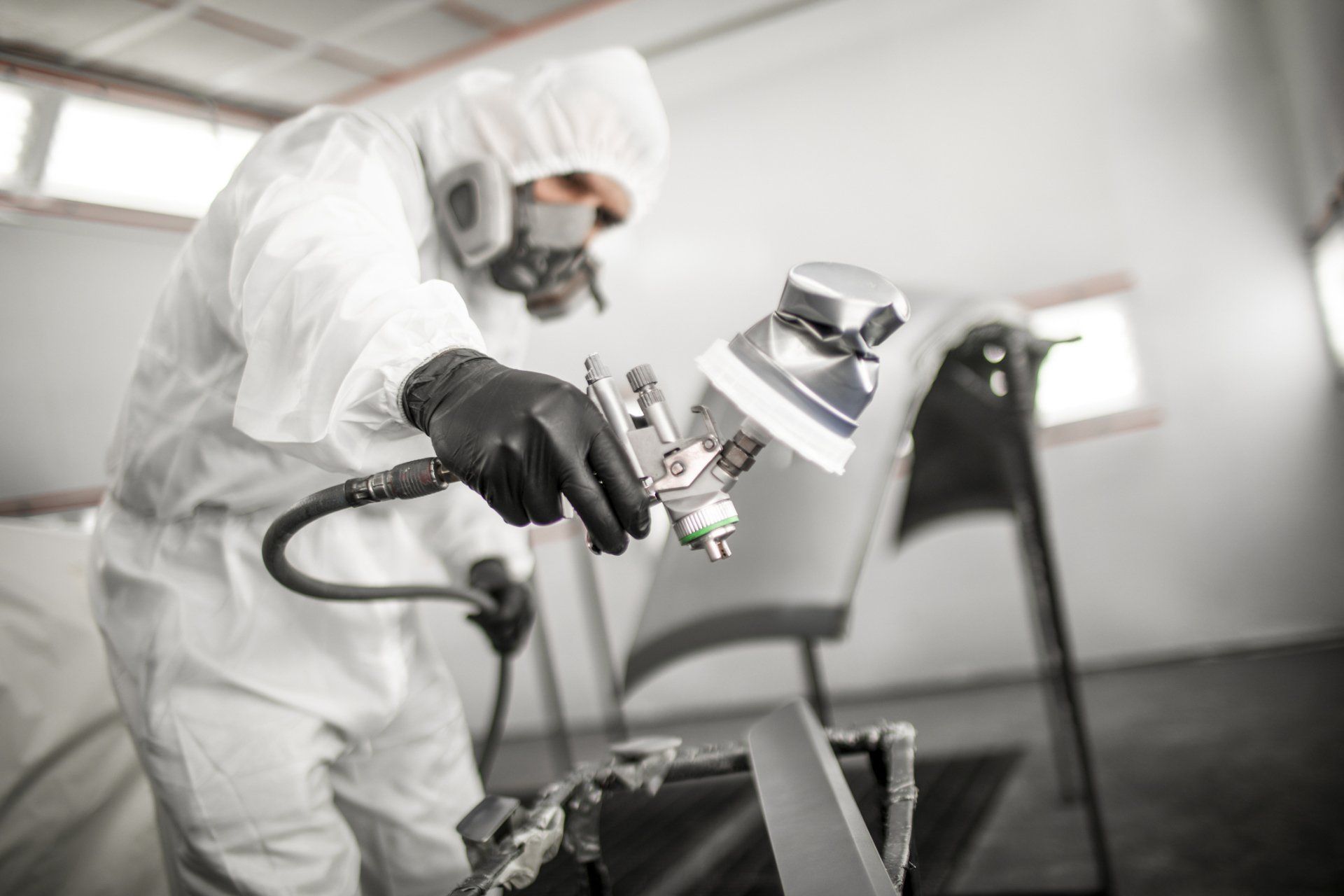 A man in a protective suit is painting a car in a garage.