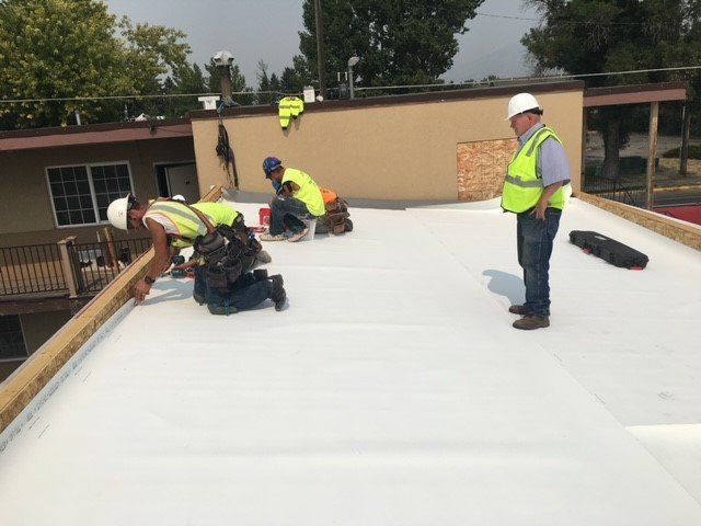 Construction workers installing a white roof on a building. One worker observes.