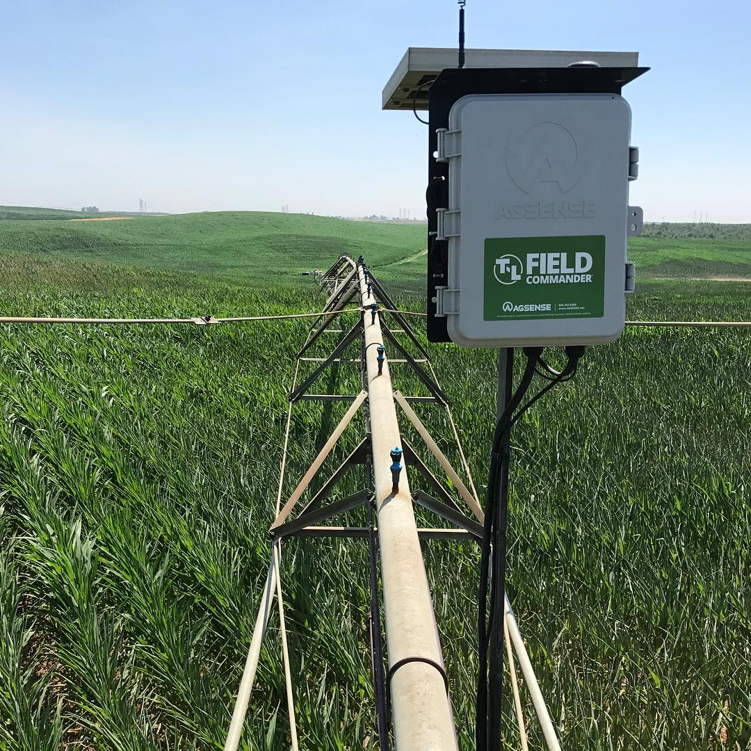 Irrigation system with mounted FieldNET sensor box in a field of green crops under a blue sky.