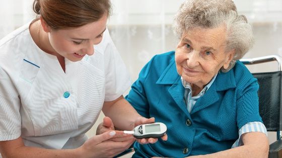 Krankenschwester misst den Blutzucker einer älteren Frau im Haus.