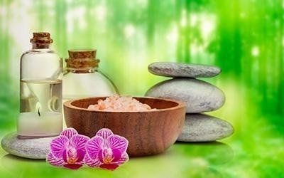 Scena della spa: bottiglie, ciotola di sale, pietre impilate, orchidee, il tutto su uno sfondo verde sfocato.