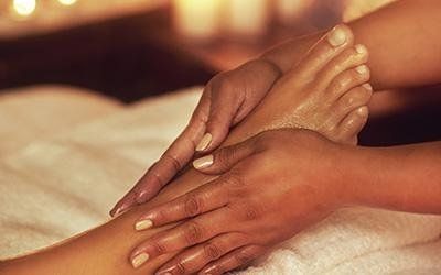 Mani che massaggiano un piede ricoperto d'olio, su un asciugamano bianco.