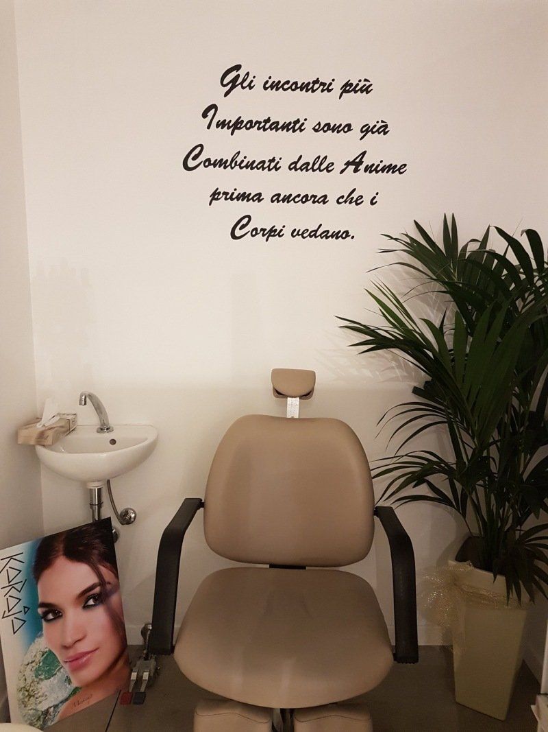 Una poltrona da salone beige, un lavandino e una scritta decorativa a parete. Accanto alla poltrona c'è una pianta in vaso.