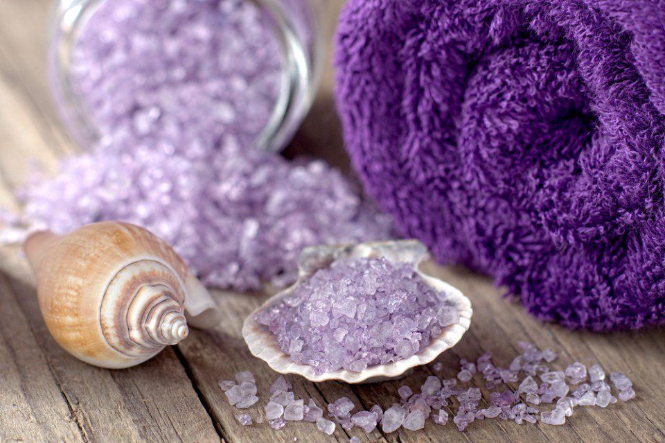 Sali da bagno viola, asciugamano e conchiglie su legno.