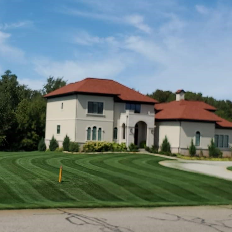 Large beige house with orange roof, neatly striped green lawn, blue sky.