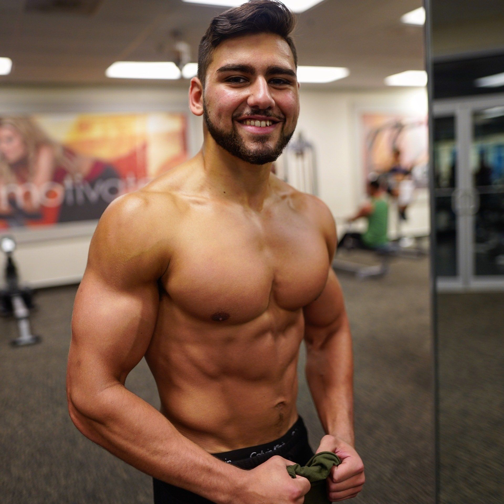 A shirtless man is standing in front of a mirror in a gym