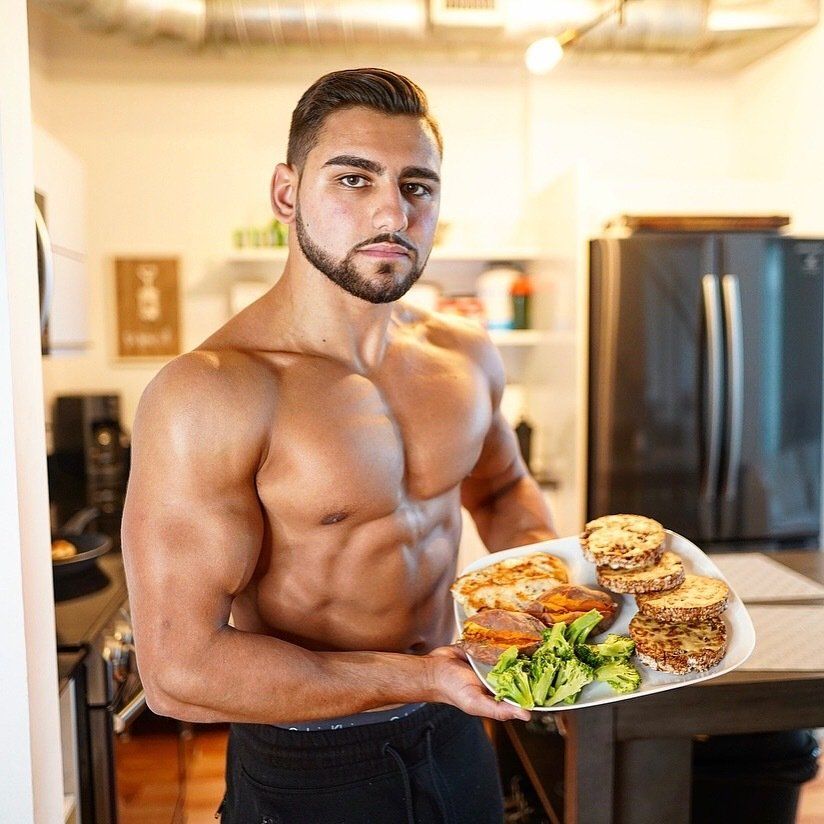 A shirtless man is holding a plate of food in a kitchen.