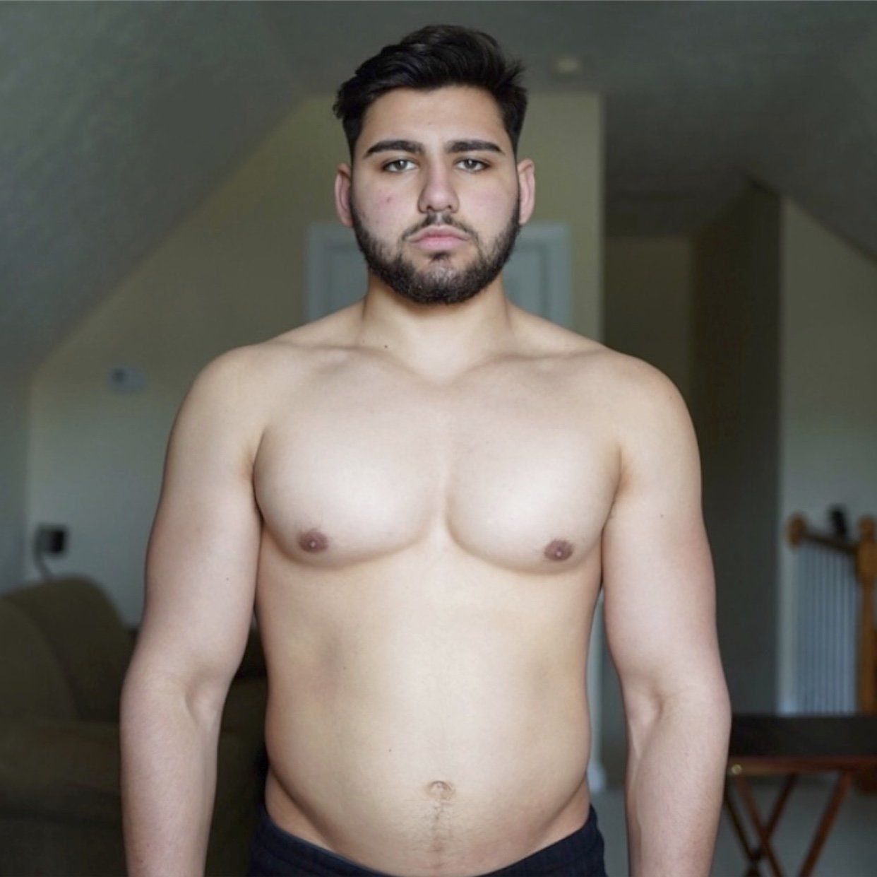 A shirtless man with a beard is standing in a living room