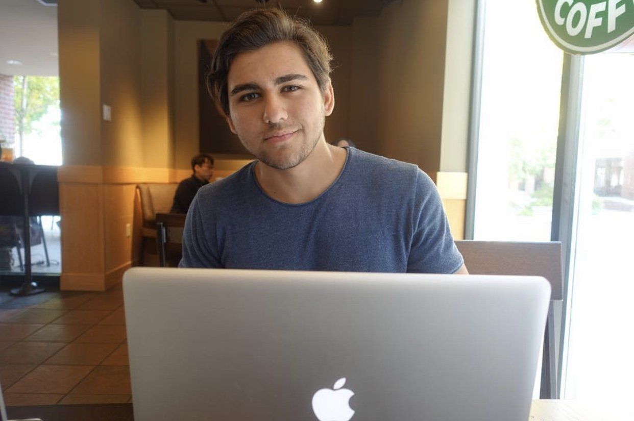 A man is sitting at a table with an apple laptop.