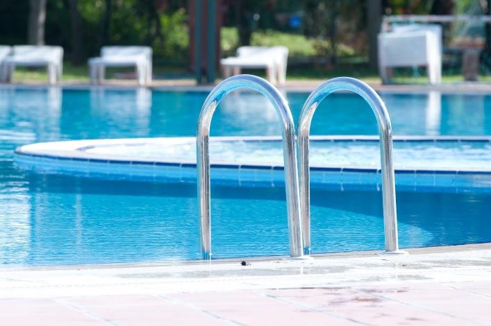 Pool with metal ladder, blue water, and white chairs in the background.