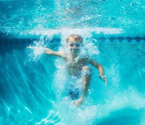 Boy underwater, splashing in a pool with arms outstretched, smiling. Blue water.
