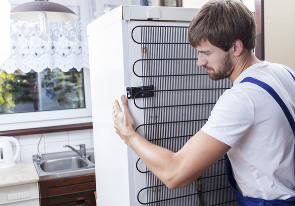 Un hombre empuja un refrigerador blanco para colocarlo en su lugar en una cocina luminosa.