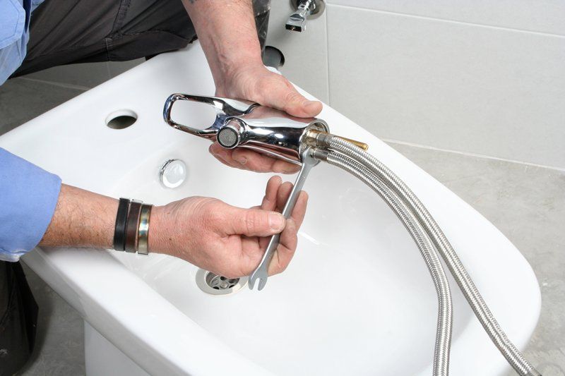 Plumber Installing Faucet On Bidet In Bathroom — KNP Plumbing and Gas — Airlie Beach, QLD Plumber Installing Faucet On Bidet In Bathroom — KNP Plumbing and Gas — Airlie Beach, QLD