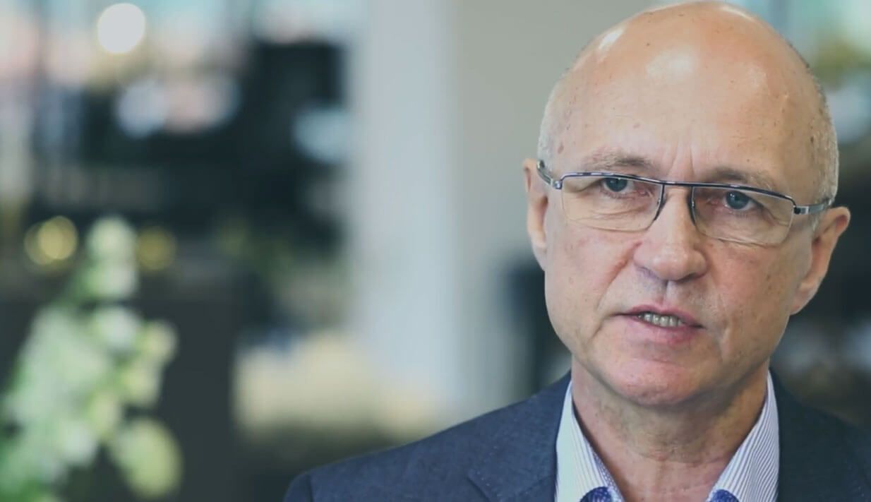 A bald man wearing glasses and a suit is talking to someone.