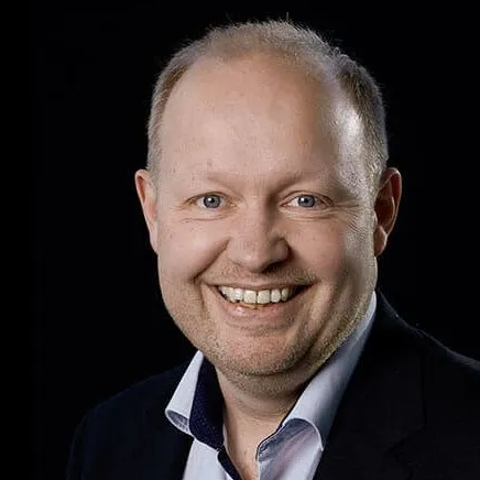 En mand i jakkesæt og skjorte smiler til kameraet.