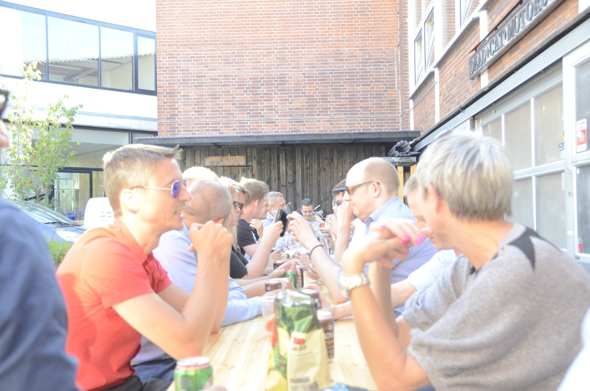 A group of people are sitting at a long table drinking beer.