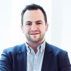 En mand i jakkesæt og stribet skjorte smiler til kameraet.