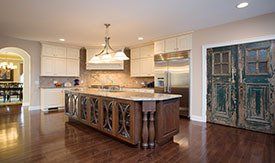 Kitchen with a large wooden island, cream cabinets, and distressed green doors. Dark wood floors and a neutral color palette.