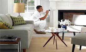 Person in white painting a fireplace in a living room with light grey walls and furniture.