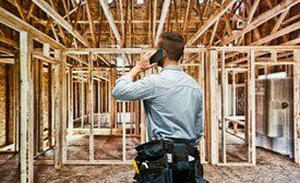 A carpenter on the phone inside a wooden house frame.