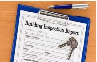 Building inspection report on a clipboard with keys and pen on a wooden surface.
