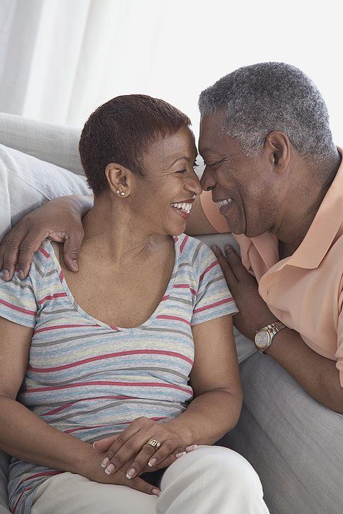 Smiling elderly couple, embrace on a sofa, touching foreheads, expressing affection.