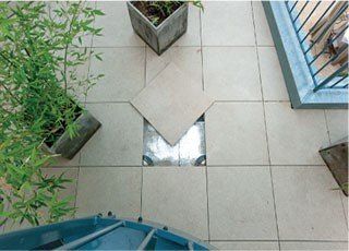 Overhead view of outdoor tiled patio with inset, removable square tile revealing a metal hatch.