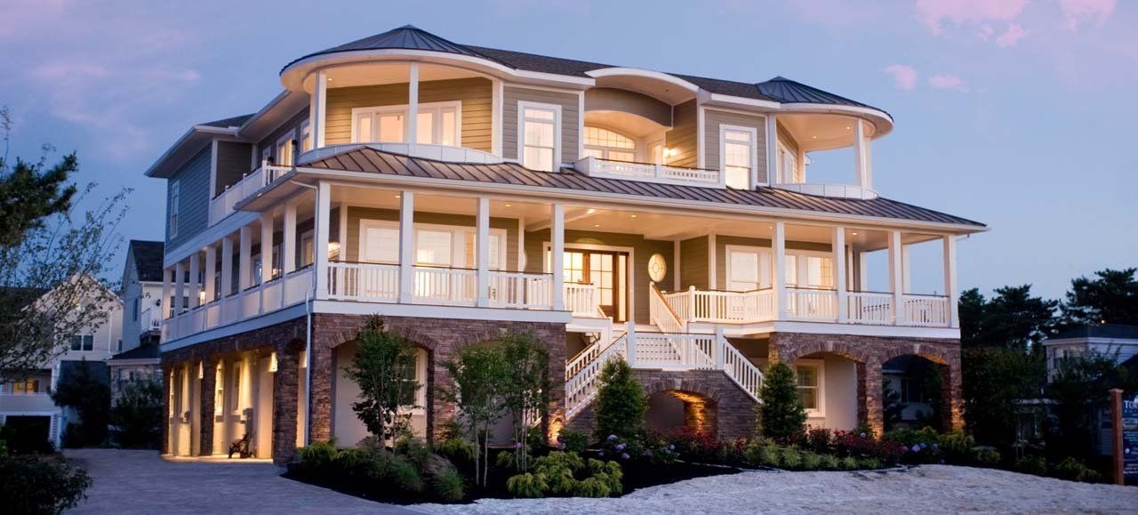 Three-story house with porch, ocean view, beige exterior, stone base, under dusk sky.