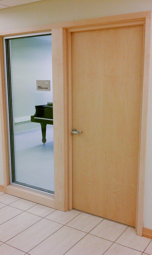 A doorway with a glass window and a wooden door. A grand piano is visible through the glass.