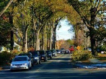 Red Car auto insurance — in West Springfield, MA Cars parked on a tree-lined street; autumn colors, sunny day.