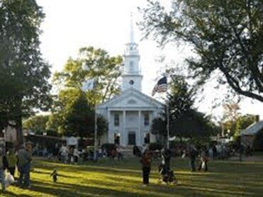 Modern office building business insurance — in West Springfield, MA White church with a steeple; people gather on a green lawn, American flag waving.